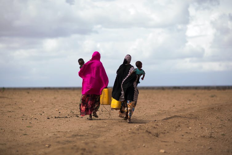 Ethiopian people walking across dry land with bags
