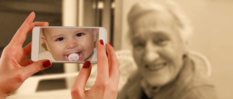 Image of elderly woman and hands holding a phone displaying a photo of a baby.