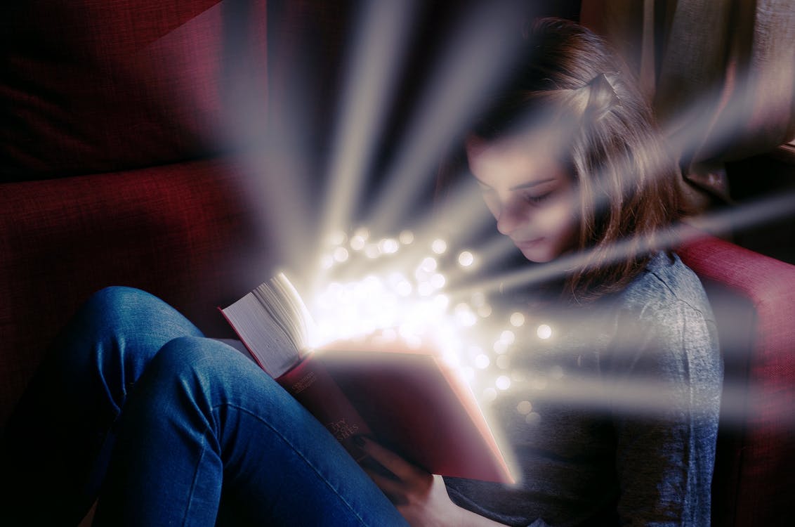 Image of girl reading a book with light rays coming out of it. 