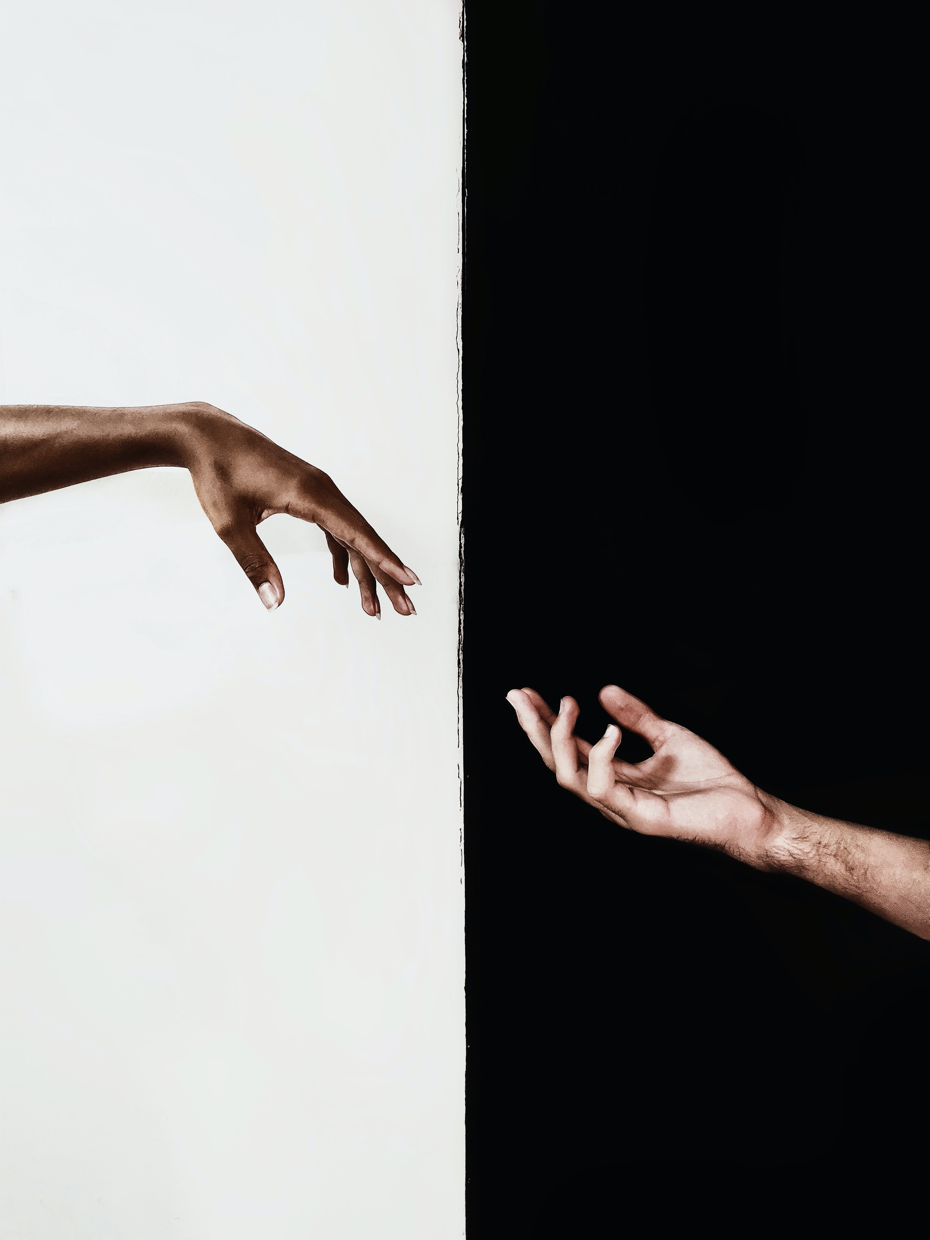 Two hands reaching for each other. Half the background is coloured black and the other half is white.