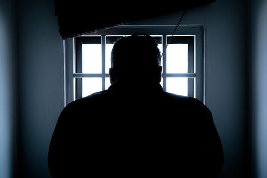 Rear view of a silhouette man in prison cell window