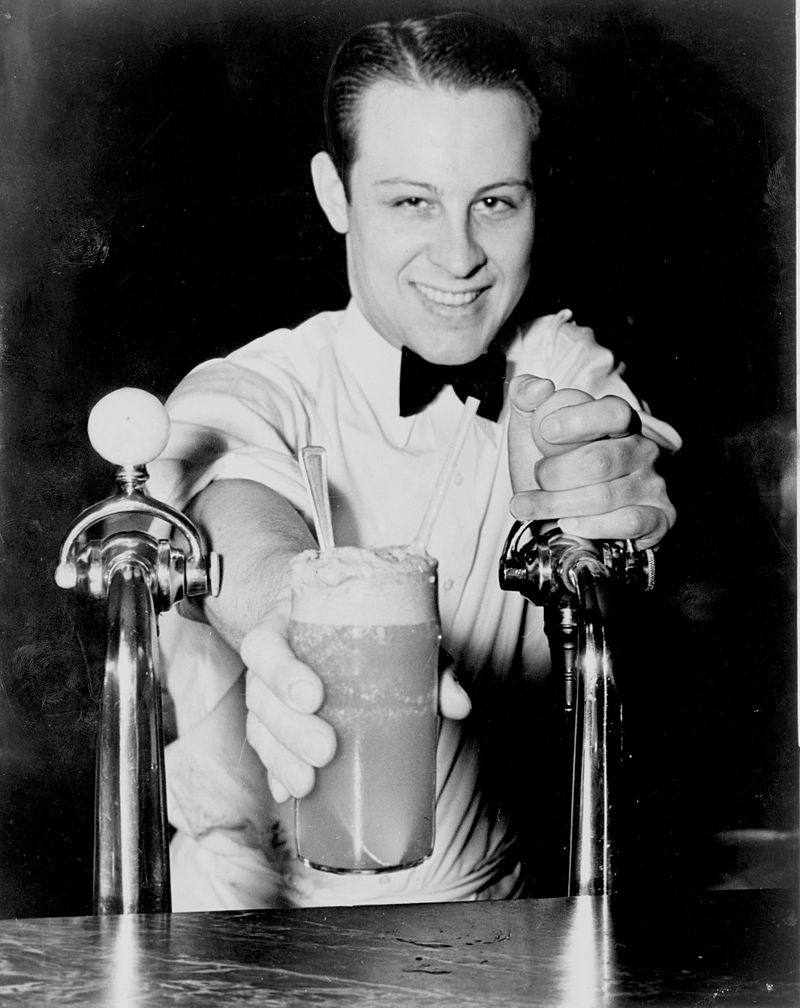 Soda jerk passing an ice cream soda between two soda fountains, New York City, 1936