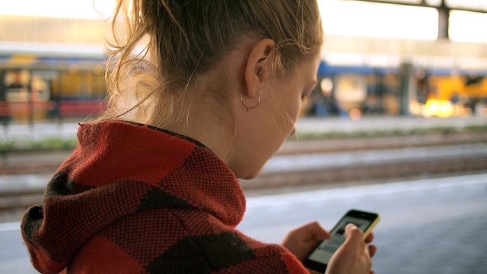 A young woman checks a smartphone on a train platform