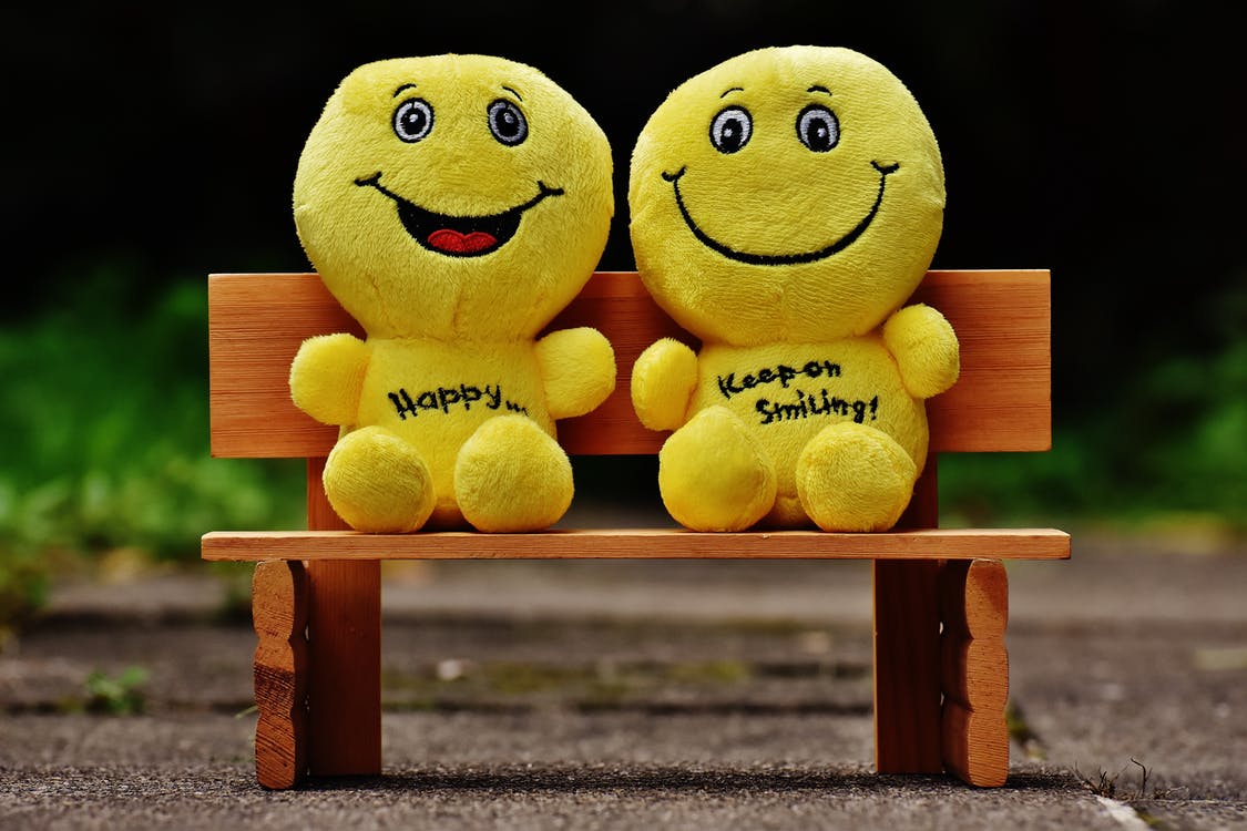 Two smiley face soft toys sitting placed alongside each other. It reads: 'Happy...keep smiling'. 