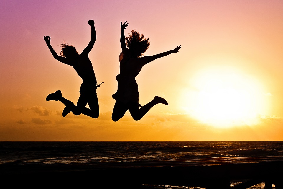 Two young people leaping with happiness on the beach with a sunset in the background. 